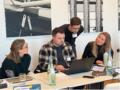 Four people gather around a laptop in a workshop