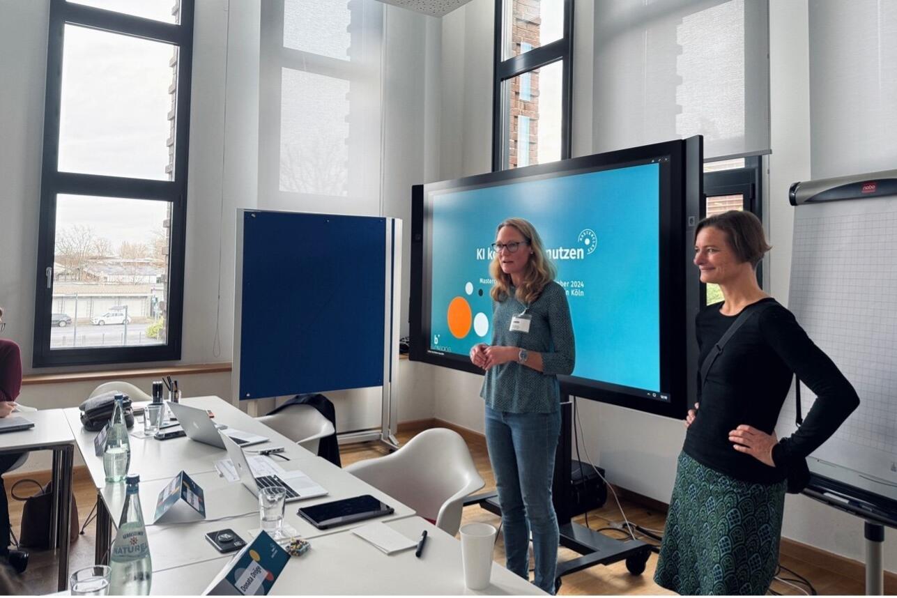 Claudia Rittel and Donata Dröge stand in front of a screen while giving a presentation on AI in journalism